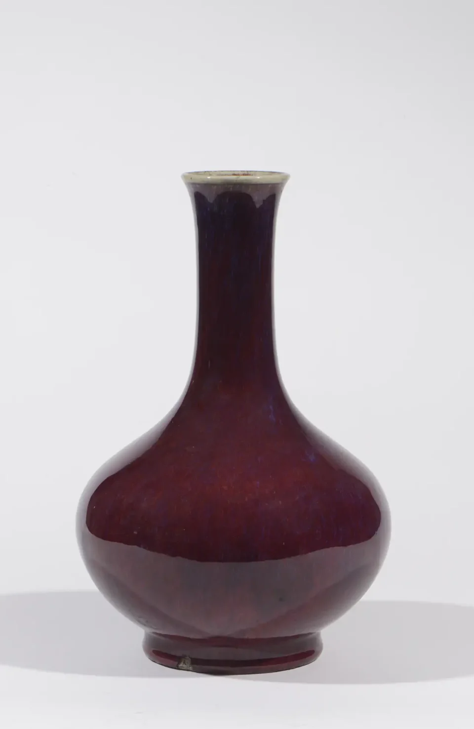 Vase pansu à long col en porcelaine et émail sang de bœuf, légèrement flammé, reposant sur un fond céladon. - CHINE - Période Jiaqing (1796-1820)